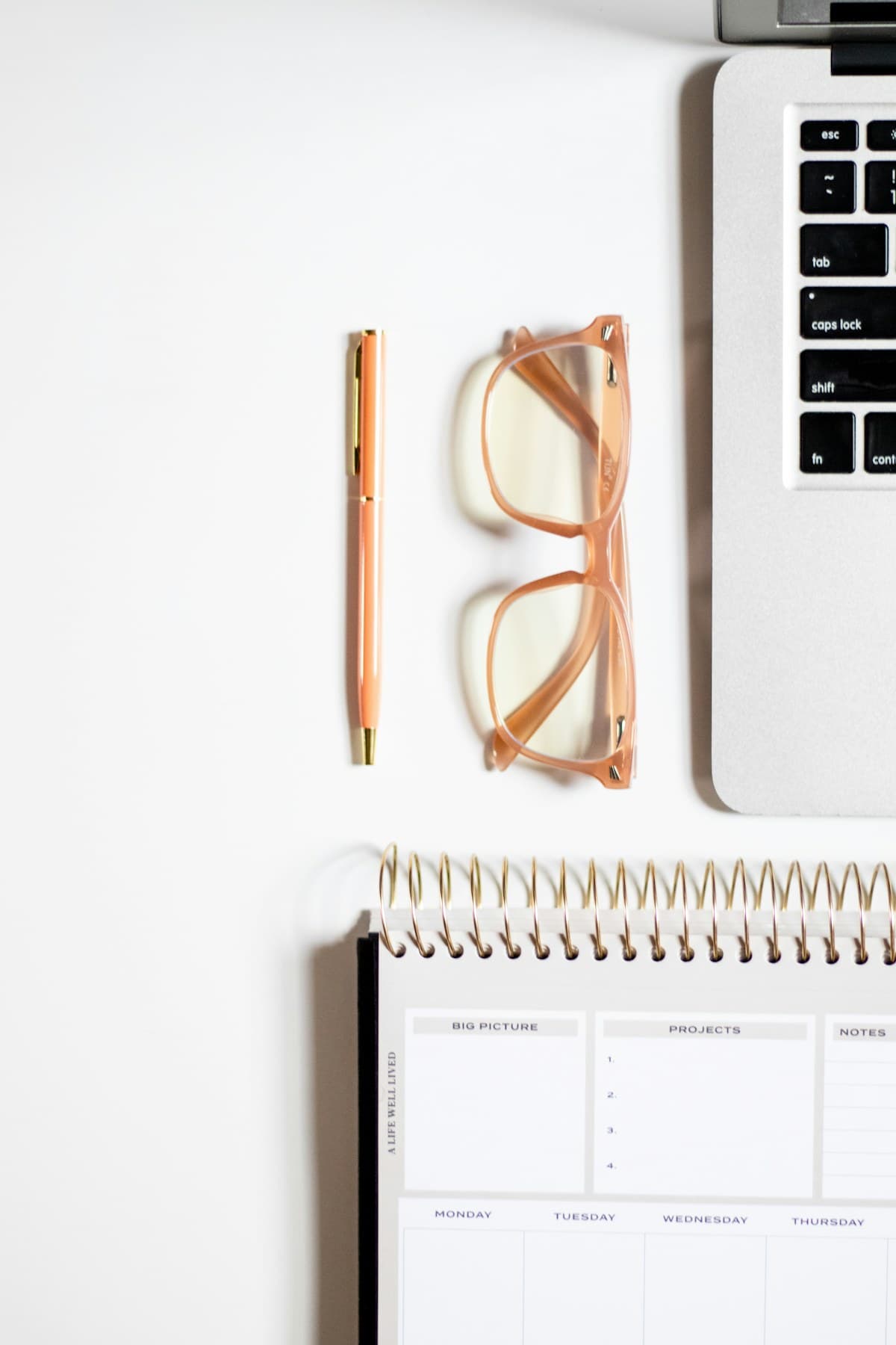 A laptop, a notebook, a pen and glasses on a white desk