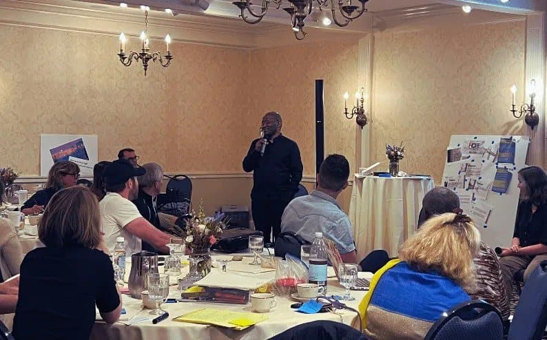 A speaker addressing a seated group in a hotel room