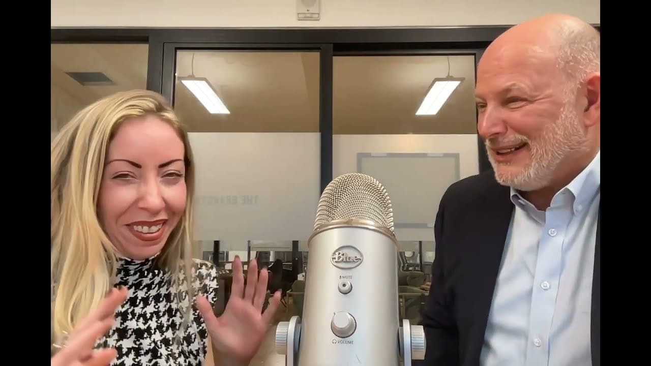 Tia Cristy and Greg Zlevor laughing on either side of a studio microphone