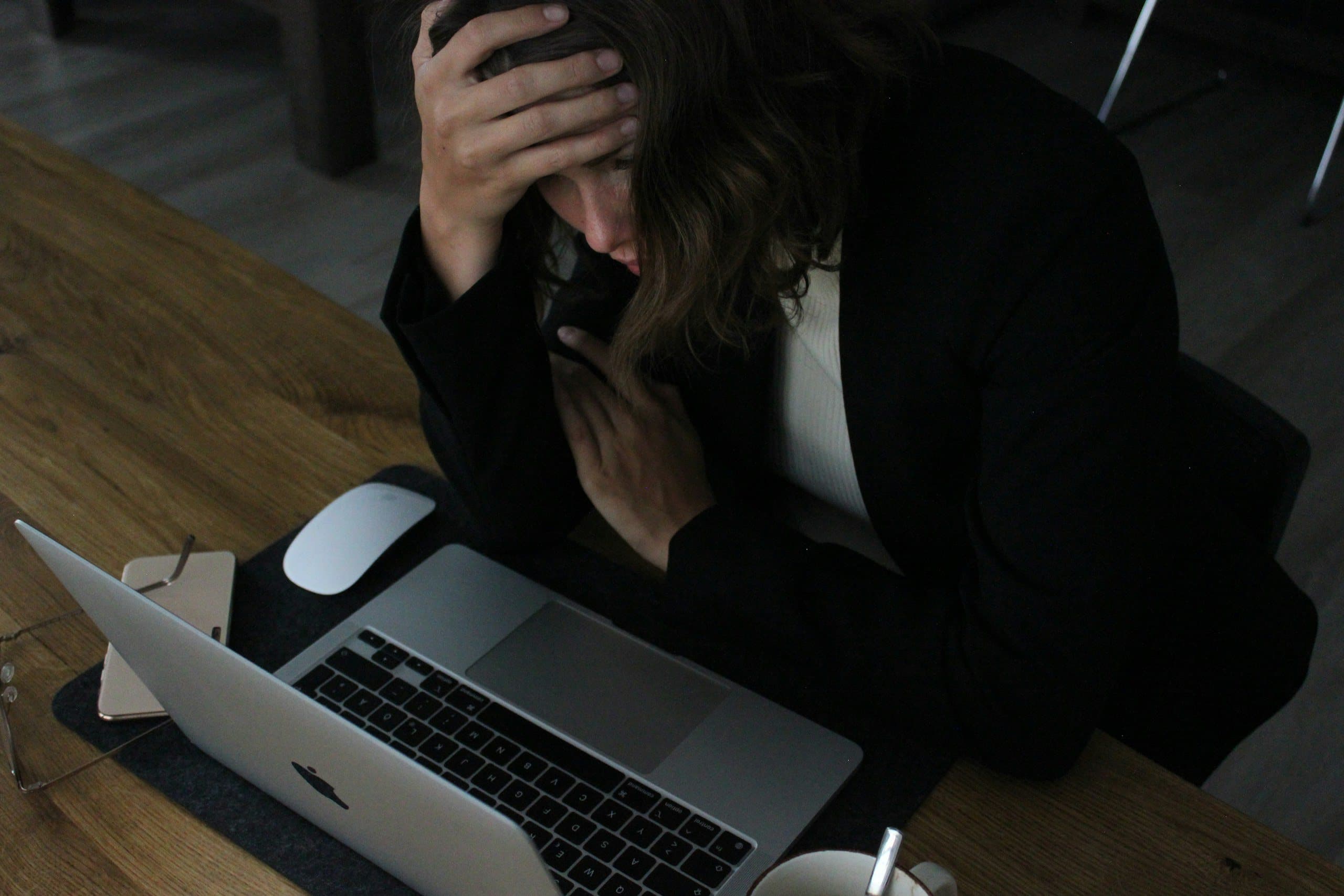 A woman with her head in her hands in front of a laptop