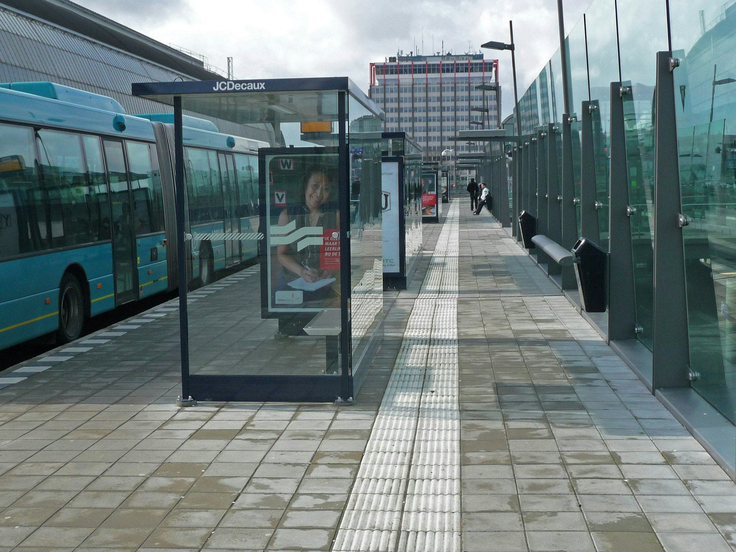 A bus waiting at a glass-sheltered stop